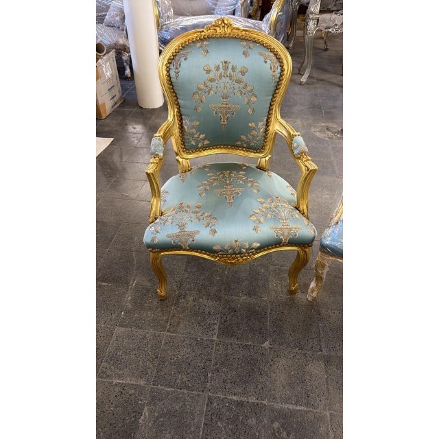 An elegant French Louis XV-style armchairs, beautifully combining an ornate gold-finished carved wood frame with...