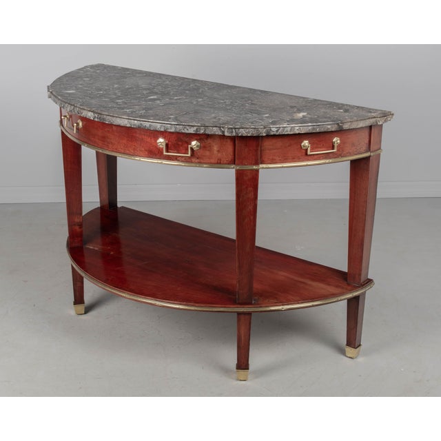 A 19th century Louis XVI style French marble top demilune console table made of solid mahogany with brass trim and sabots....