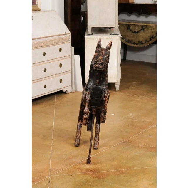 A French carved wooden carousel horse sculpture from the late 19th century, with dark paint, glass eyes, supporting bar...