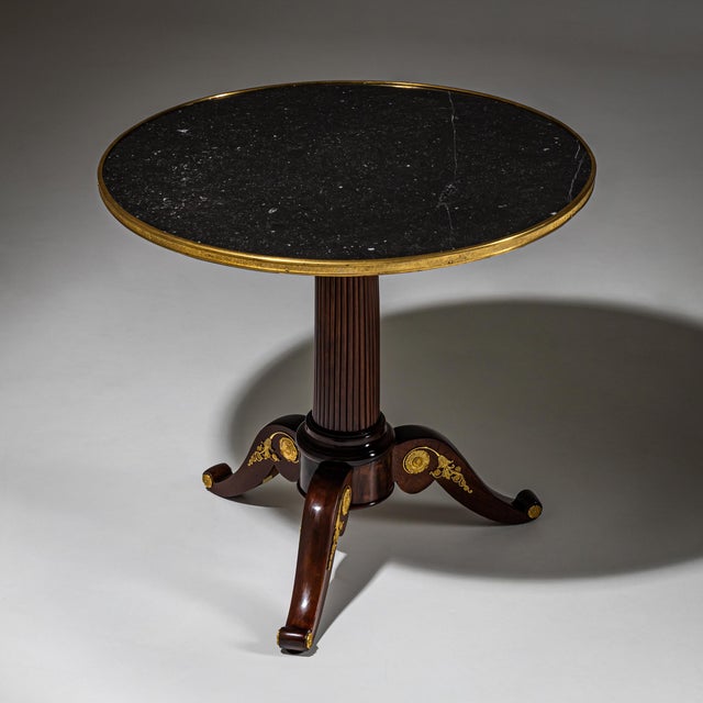 Mahogany Guéridon with a round top in black stone, framed by a profiled brass edge. The fluted column stands on a...