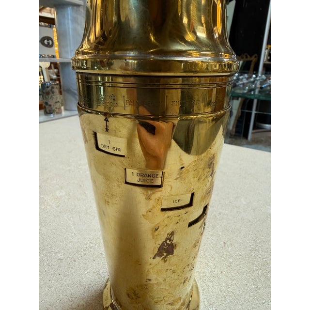 Elegant vintage brass cocktail shaker featuring integrated recipe windows on the body, a clever mid-century design that...