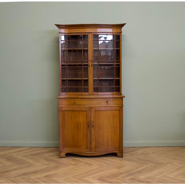 A well-made 1930s oak display cabinet in the Georgian Revival style, featuring a serpentine front, curved cornice,...