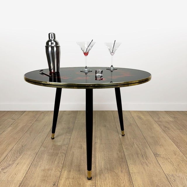 This sublime tripod coffee table dates from the 1950s. Its large, round glass top is adorned with red flame patterns that...