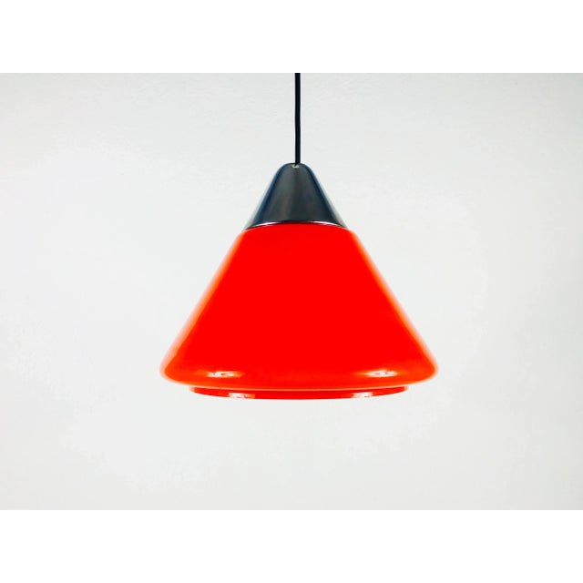 A red hanging lamp by Peill and Putzler made in Germany in the 1970s. It has a red glass shade in the shape of a cone. The...
