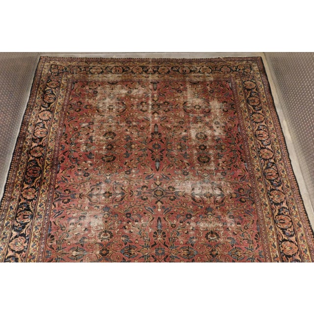 Distressed antique Persian rug in floral style. Rust/pink field within blue border. 10'8"x 14'
