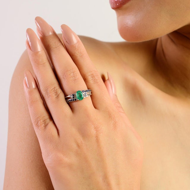 This elegant ring is crafted in 925 sterling silver and features a 7x5 mm oval emerald (0.8 ct), complemented by subtle...