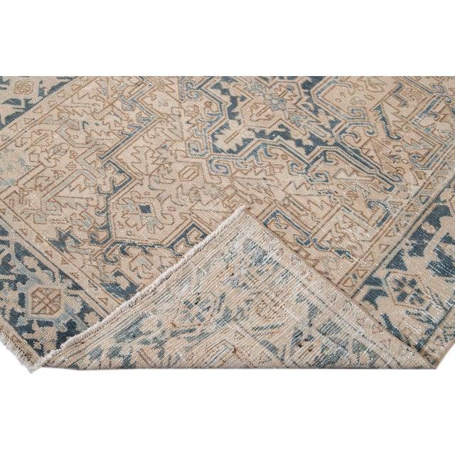 Beautiful antique Persian Heriz hand-knotted wool rug with a beige field. This Heriz rug has a blue frame and accents in...