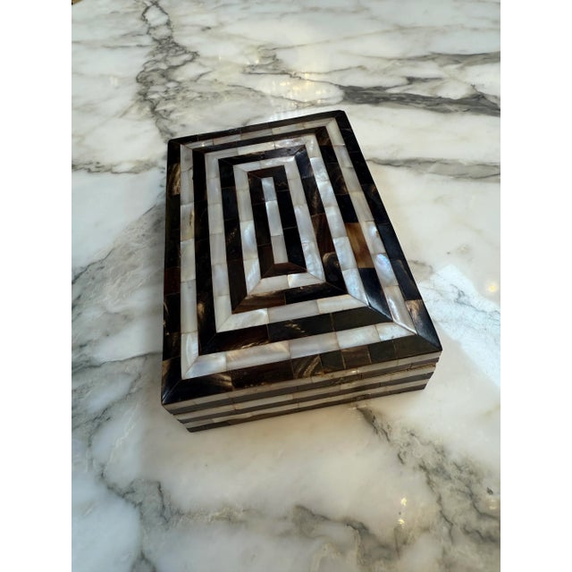 This elegant rectangular box showcases a striking geometric design created from alternating strips of dark horn and...