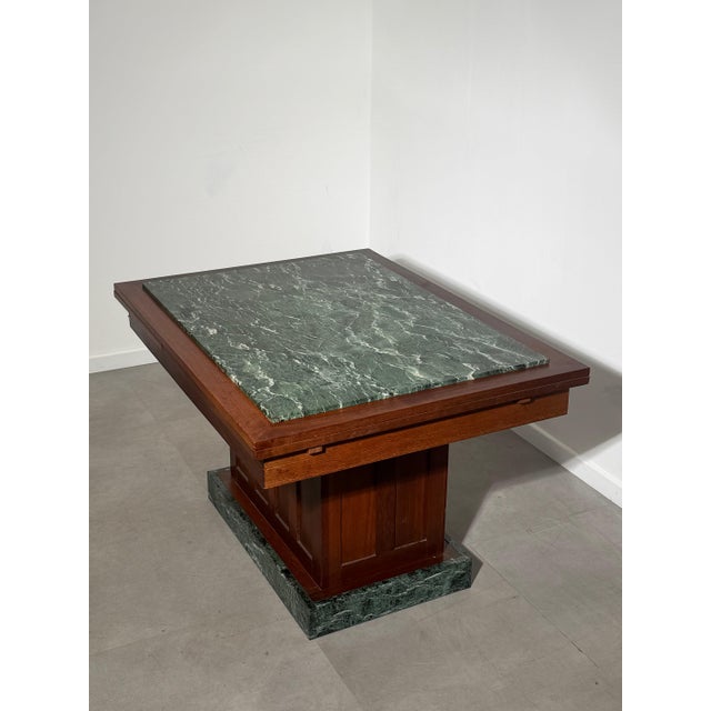 Elegant Art Deco dining table featuring a striking green marble top framed by rich walnut-toned wood. The table stands on...
