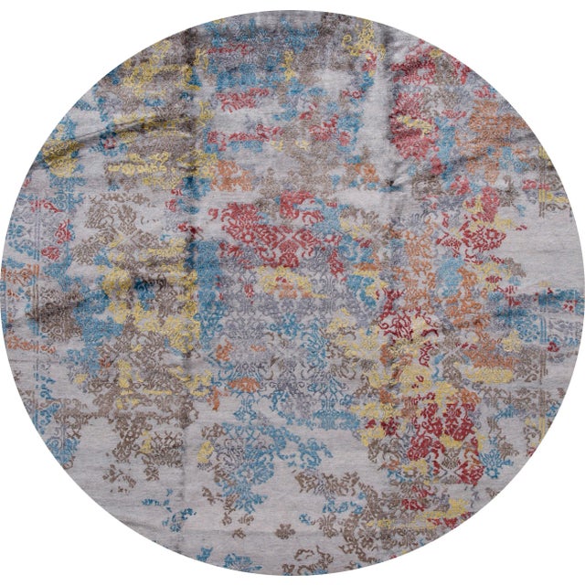 A contemporary Indian silk rug with an all-over abstract grey, blue, red and yellow design overlaying a grey traditional...