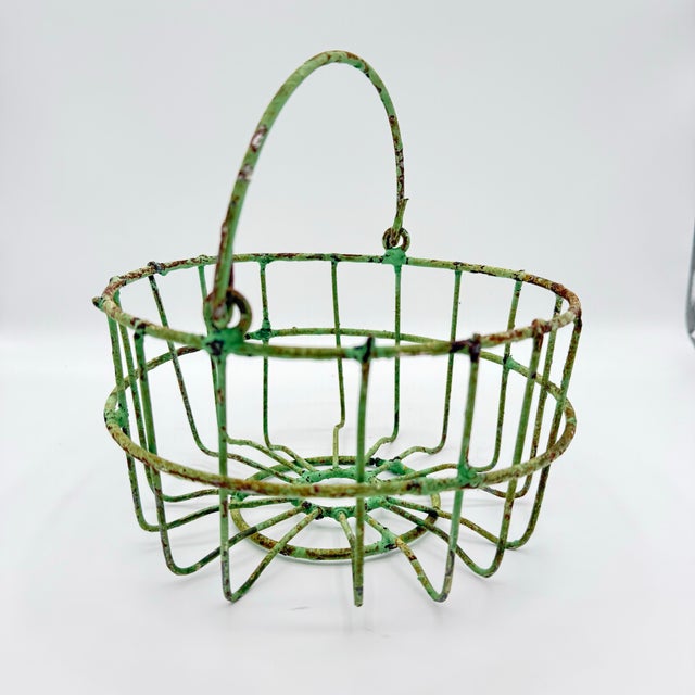 A character-rich vintage wire egg basket with a naturally aged green verdigris patina. The open wire form and swing handle...