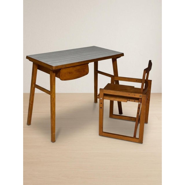 A distinctive mid-century writing desk with a compact rectangular top, slender tapered legs, and an integrated drawer...