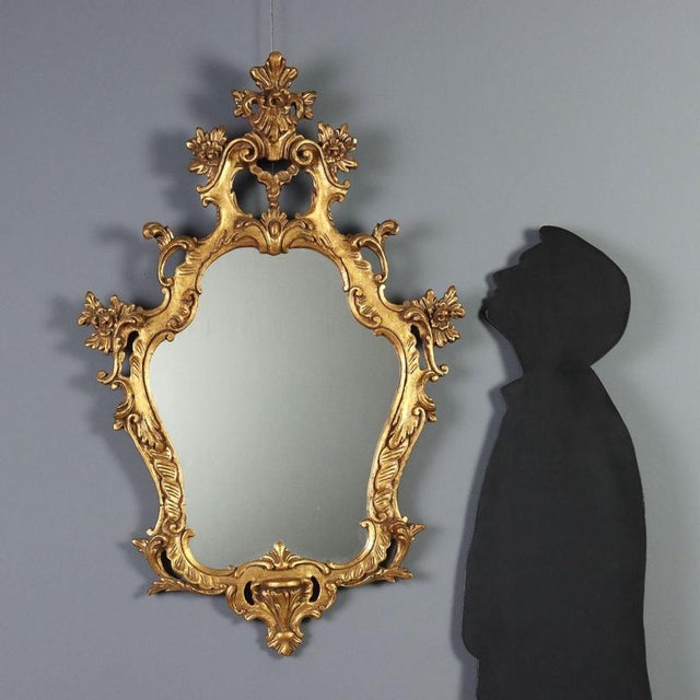 Giltwood mirror, crafted in Barocchetto style, originating from 20th century Italy. The frame features an elaborate...