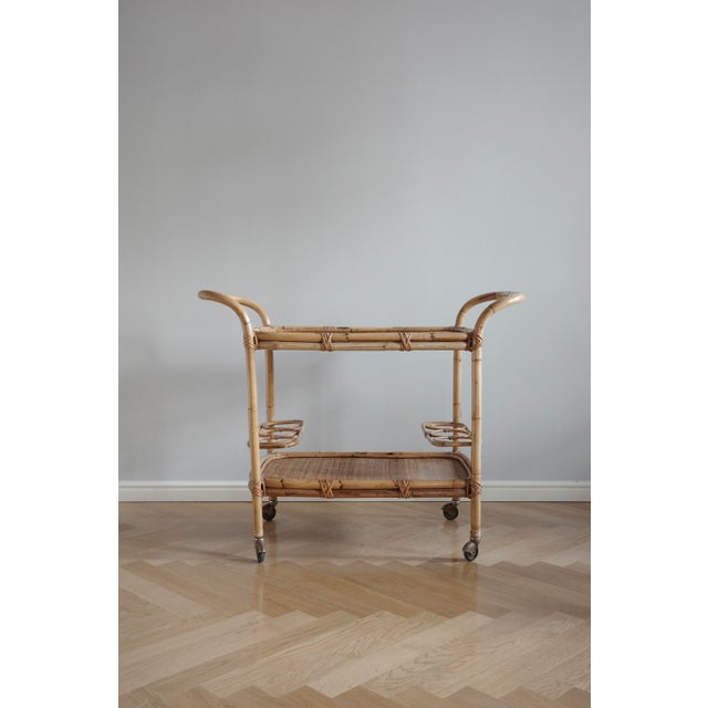 A 1950s bar cart on wheels, made of bamboo and rattan with two levels and bottle holders makes it a stylish, functional...
