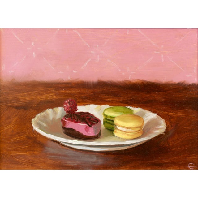 This oil painting features a delicate arrangement of colorful macarons and a raspberry-topped dessert on a white plate,...