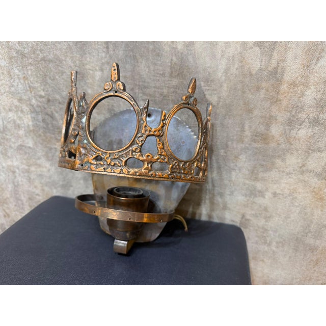 A vintage metal wall sconce with an openwork crown design, circular openings, and pointed ornamental details rising along...