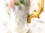 This is a white unmarked, hand painted and signed chocolate pot or teapot. It has pink flowers, smaller blue flowers and...