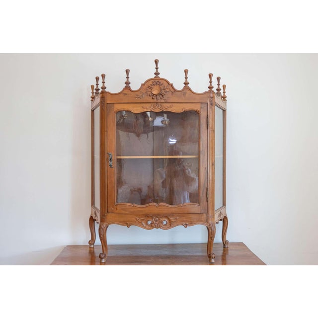 A French Louis XV style walnut display cabinet from the 19th century, with glass door, carved motifs and petite finials....