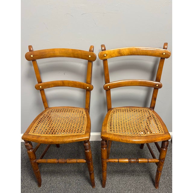 A charming pair of antique ladder back side chairs, modest in scale yet brimming with character. Each features a finely...