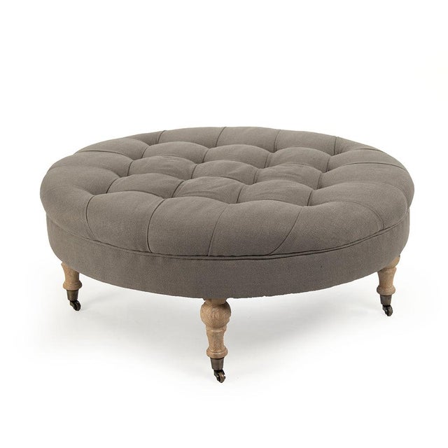 The Maison Tufted Round Ottoman from Zentique features a generous round button-tufted top on turned wood legs with brass...