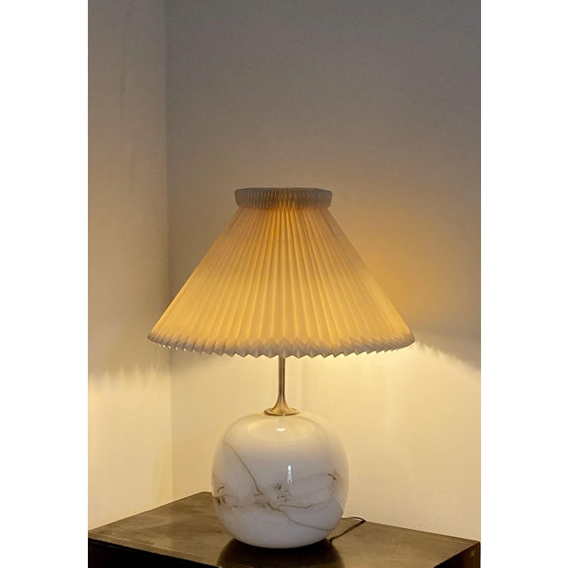 The marbled glass base glows from within, its swirling veins of gold and white catching the light like a fragment of...