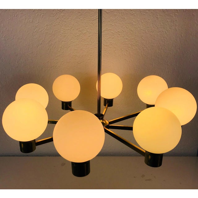 Mid-Century Modern chandelier made in the 1960s. It has eight metal arms, each with an opaline glass shade in...