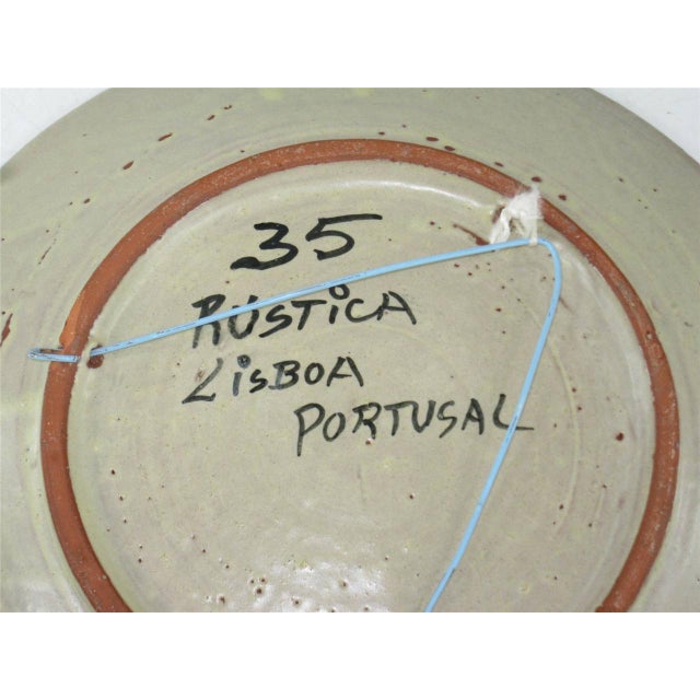 This is an unmarked beige ceramic platter, hand-painted and 12" in size. It is from Portugal, signed by Rustica Lisboa,...