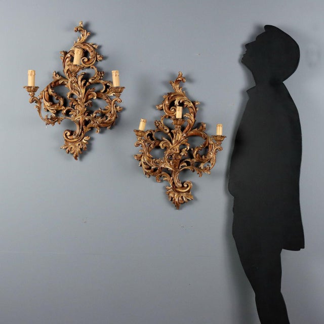 A pair of perforated and carved wooden wall lamps featuring an elaborate design of leaves and swirls. The lacquered and...