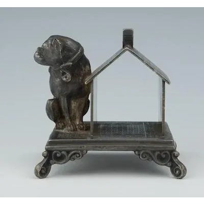 A Victorian Figural Bulldog Napkin Holder Seated by his dog house, the bulldog casts his gaze warily over one shoulder,...