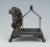 A Victorian Figural Bulldog Napkin Holder Seated by his dog house, the bulldog casts his gaze warily over one shoulder,...