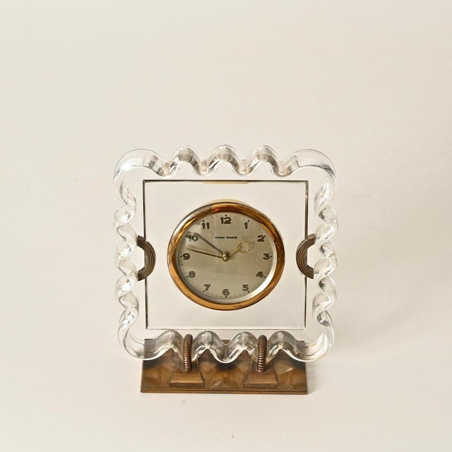 Elegant and unique Art Deco table clock featuring a sculptural clear celluloid frame with a solid brass base and accents....
