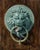 This artwork features a striking juxtaposition of a lion's head door knocker and a woodpecker perched on its ring,...