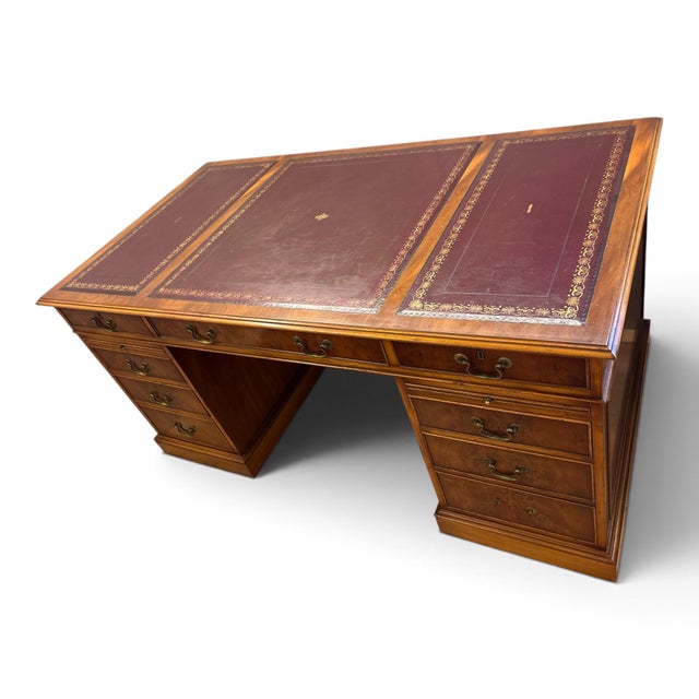 A large writing desk with two drawer pedestals and a red leather top with a gold-tooled border. Drawers with brass handles...