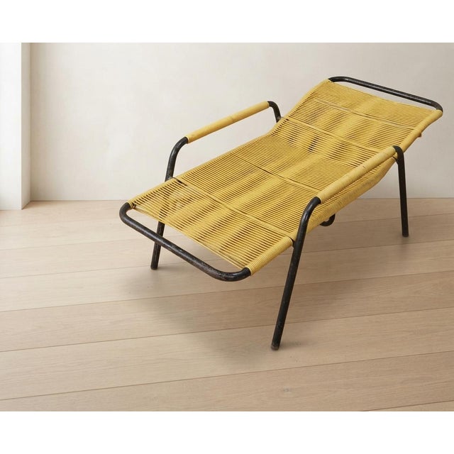 A distinctive vintage lounge chair from the 1970s, featuring a tubular metal frame with a flexible woven yellow cord seat...