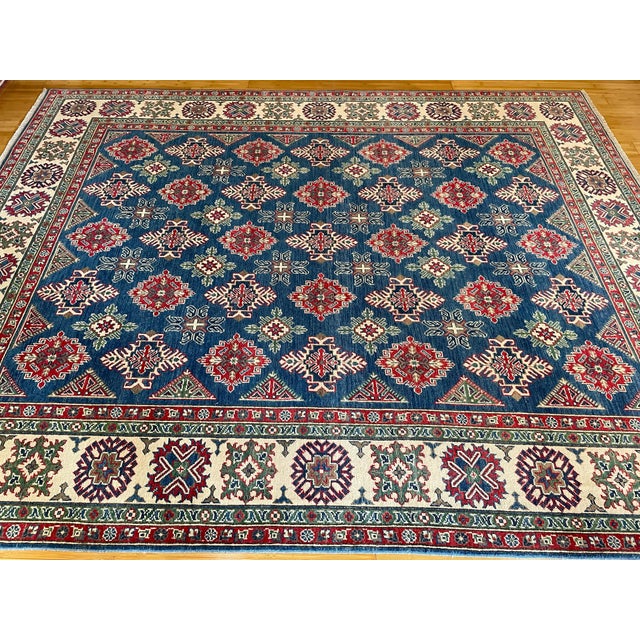 This is a Caucasian Kazak-style rug, featuring a vivid blue field adorned with bold geometric medallions and tribal star...