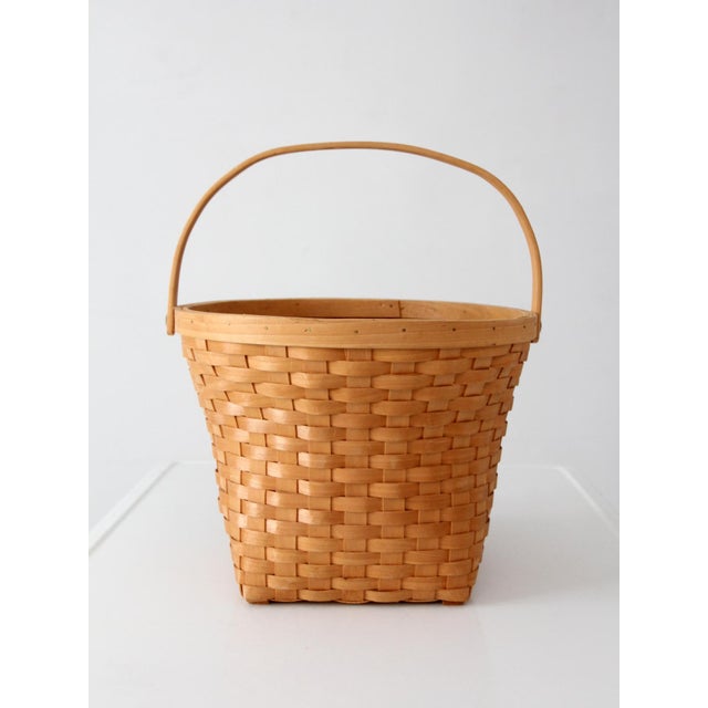 A vintage splint weave basket featuring a bentwood bail handle and a warm honey-toned finish. The gently tapered square...