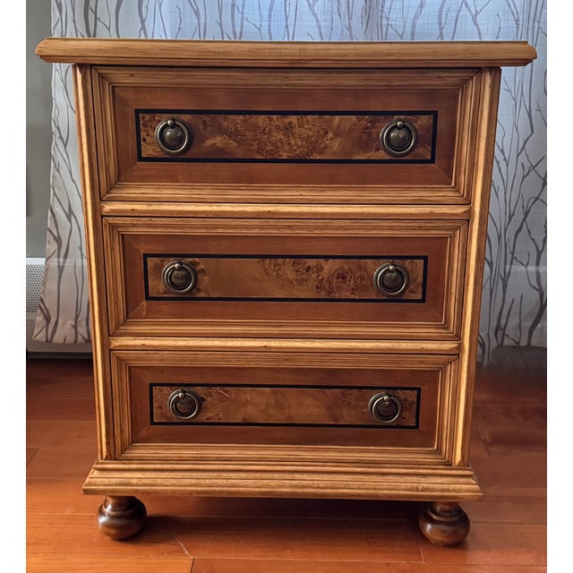 A distinctive vintage three-drawer chest featuring richly figured burl wood veneer panels framed by contrasting dark...