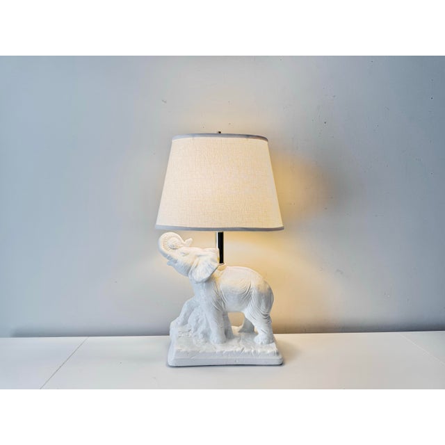 Vintage plaster elephant table lamp with brass accents. The piece is in a white lacquer and paired with a tapered cotton...