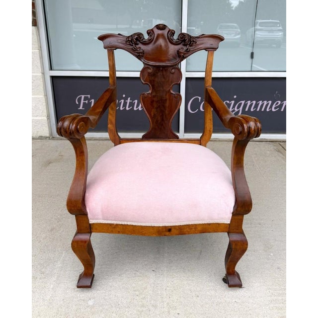 This Victorian walnut armchair features an ornately carved crest rail with scrolling floral details and a decorative...
