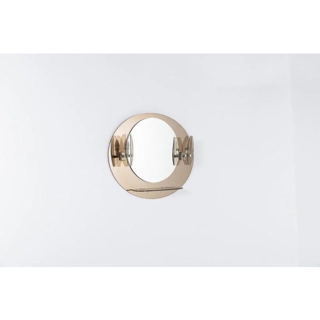 Mid-Century beveled mirror mounted onto smoked glass background, equipped with sconces and a smoked glass shelf. Condition...