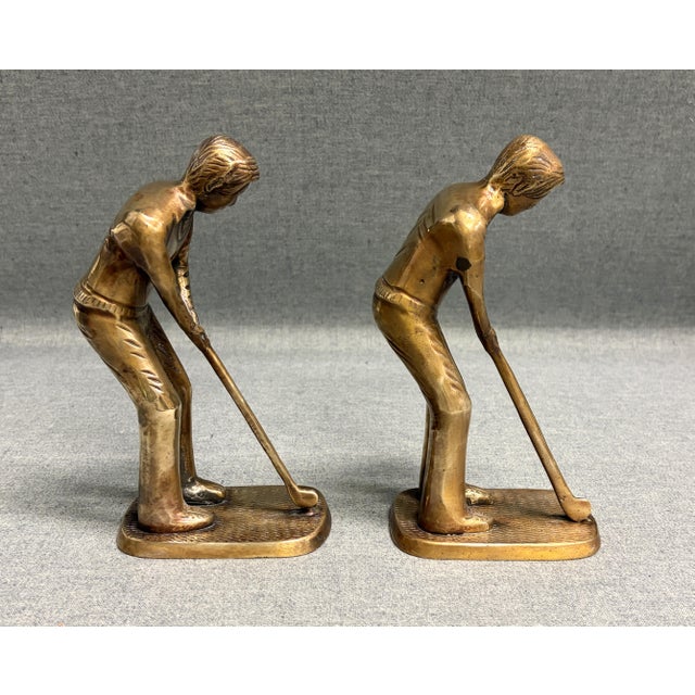 A vintage pair of brass golf player bookends. The mid-century set displays detailed design in an aged gold-tone finish....