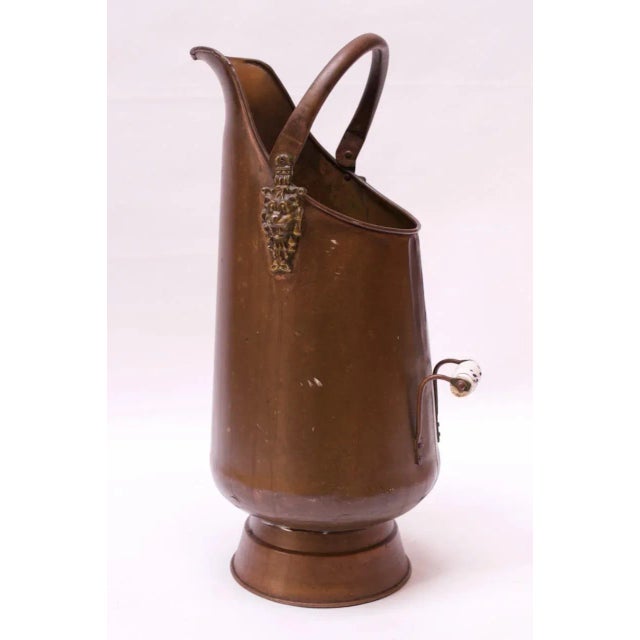 This uniquely tall brass coal scuttle / coal pail features a delft handle and ornate lion detail on both sides (circa...