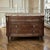 An antique French Louis XVI commode crafted from rich walnut and crowned with a luxuriously veined marble top in shades of...