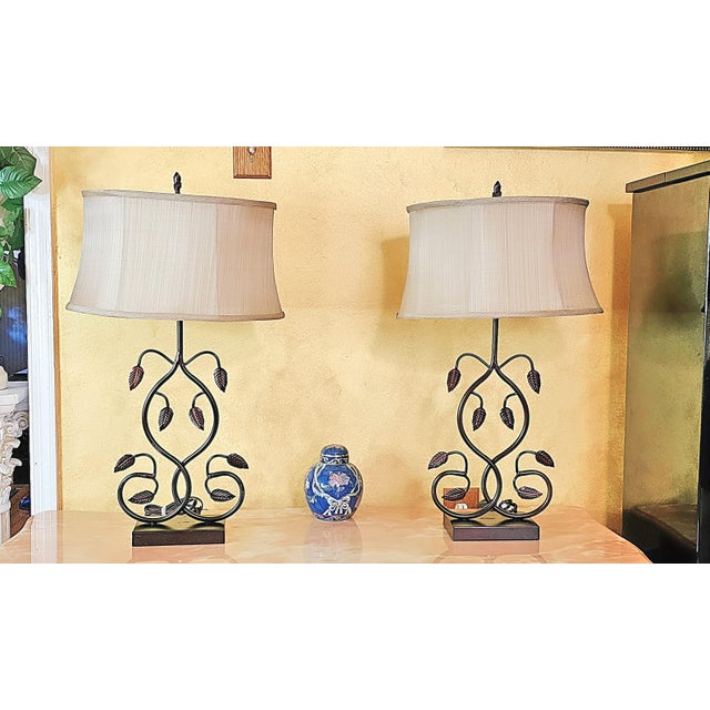 This unique pair of vintage table lamps features wrought iron frames designed with gracefully curved vines and embossed...