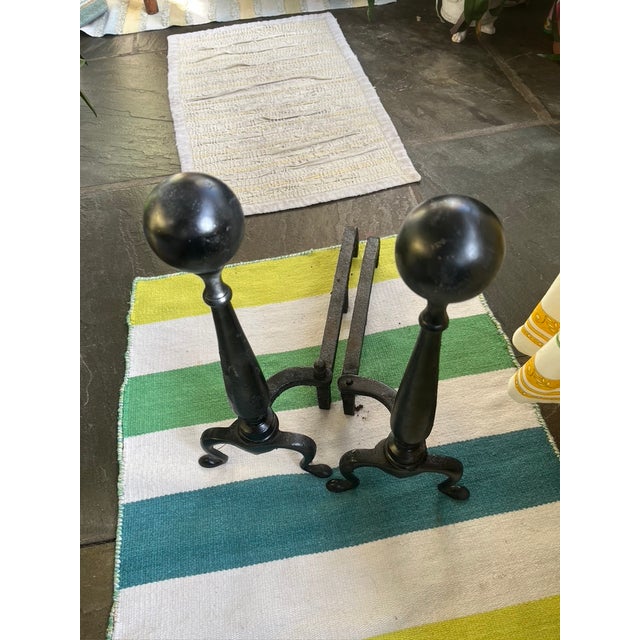 A pair of antique cast iron Federal style andirons with tall ball-top finials, cabriole legs and scrolled feet. Set on a...