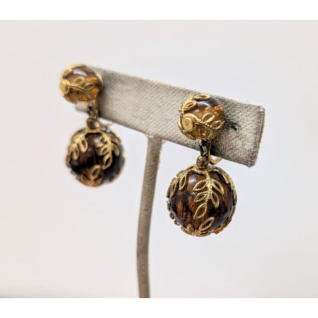 Early 1950s goldtone filigree and striated faux-tortoise resin beads drop clip back earrings. Marked crown "TRIFARI."...