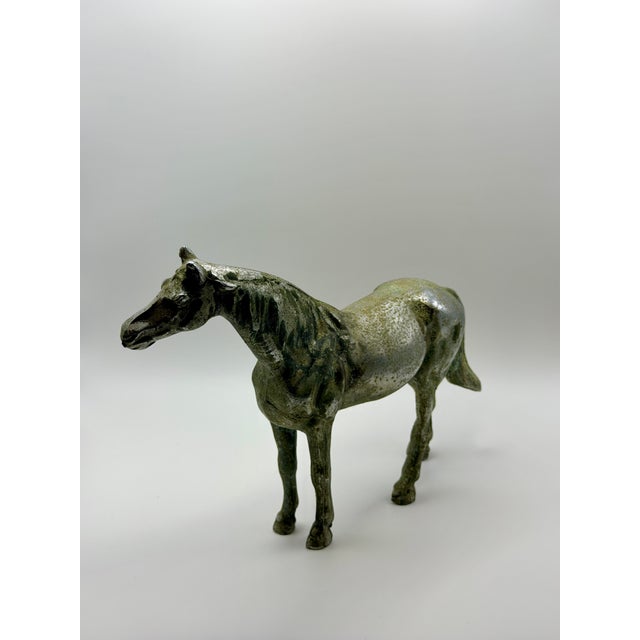 Elegant vintage cast metal horse sculpture featuring a graceful standing pose and a beautifully aged silver-toned finish....