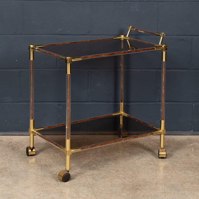 An elegant Italian bar trolley dating from the 1970s. The piece features a refined structure in polished brass with clear...