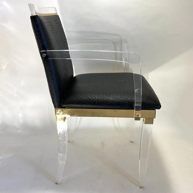 DETAILS A set of four vintage lucite and brass dining chairs with black ostrich leather backs and seats. In the style of...