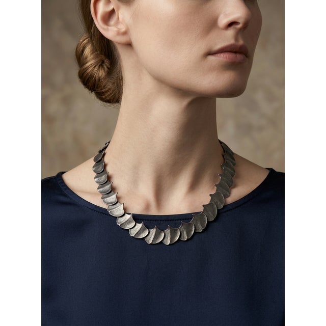 This articulated metal collar necklace is a striking statement piece that beautifully balances structured geometry with...